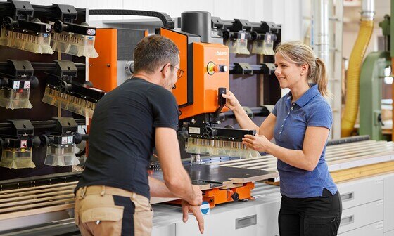 A Blum expert shows a cabinet maker how to change the drilling head on the MINIPRESS top drilling and insertion machine.