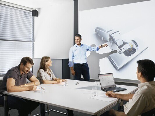 Man presenting Blum Hinge infront of group of people in boardroom
