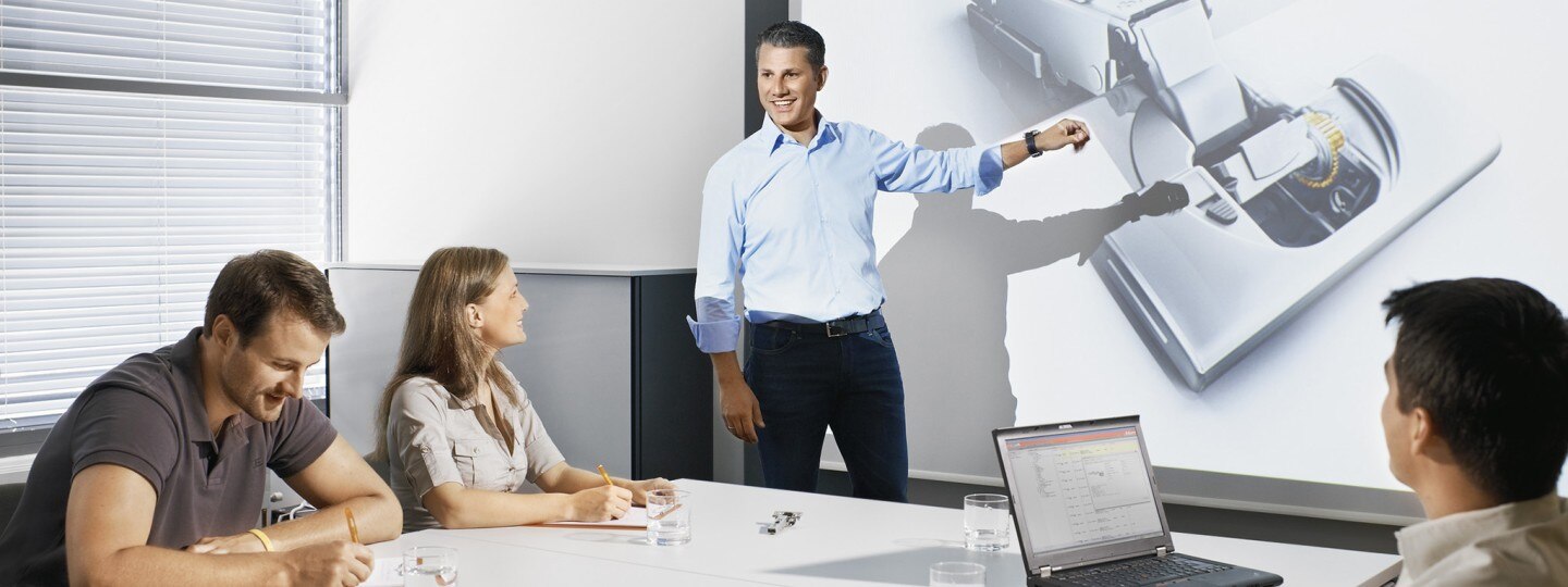 Man presenting Blum Hinge infront of group of people in boardroom